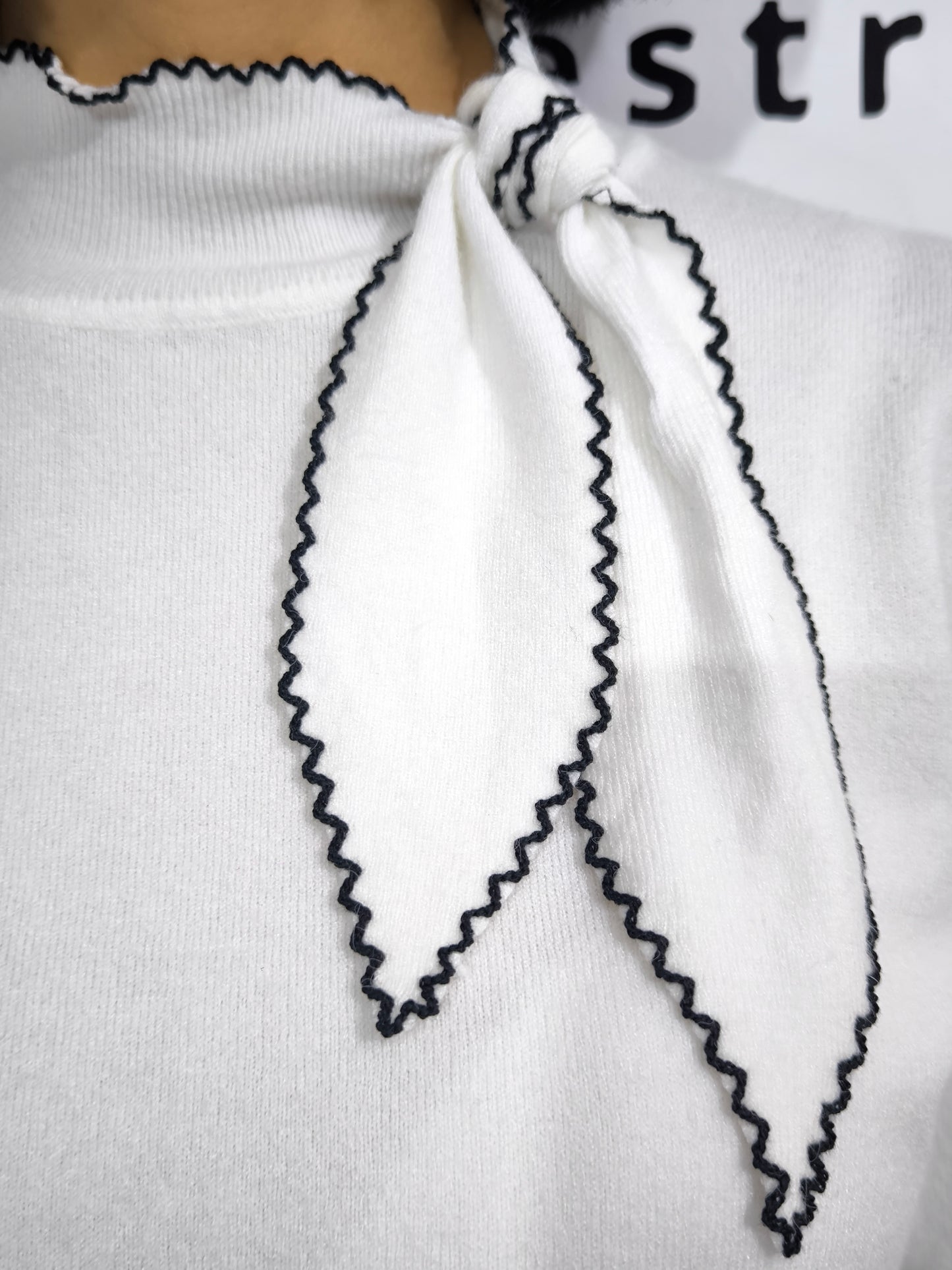 Maglia bianca con fiocco al collo e bordo ricamato in nero, elegante e raffinata.