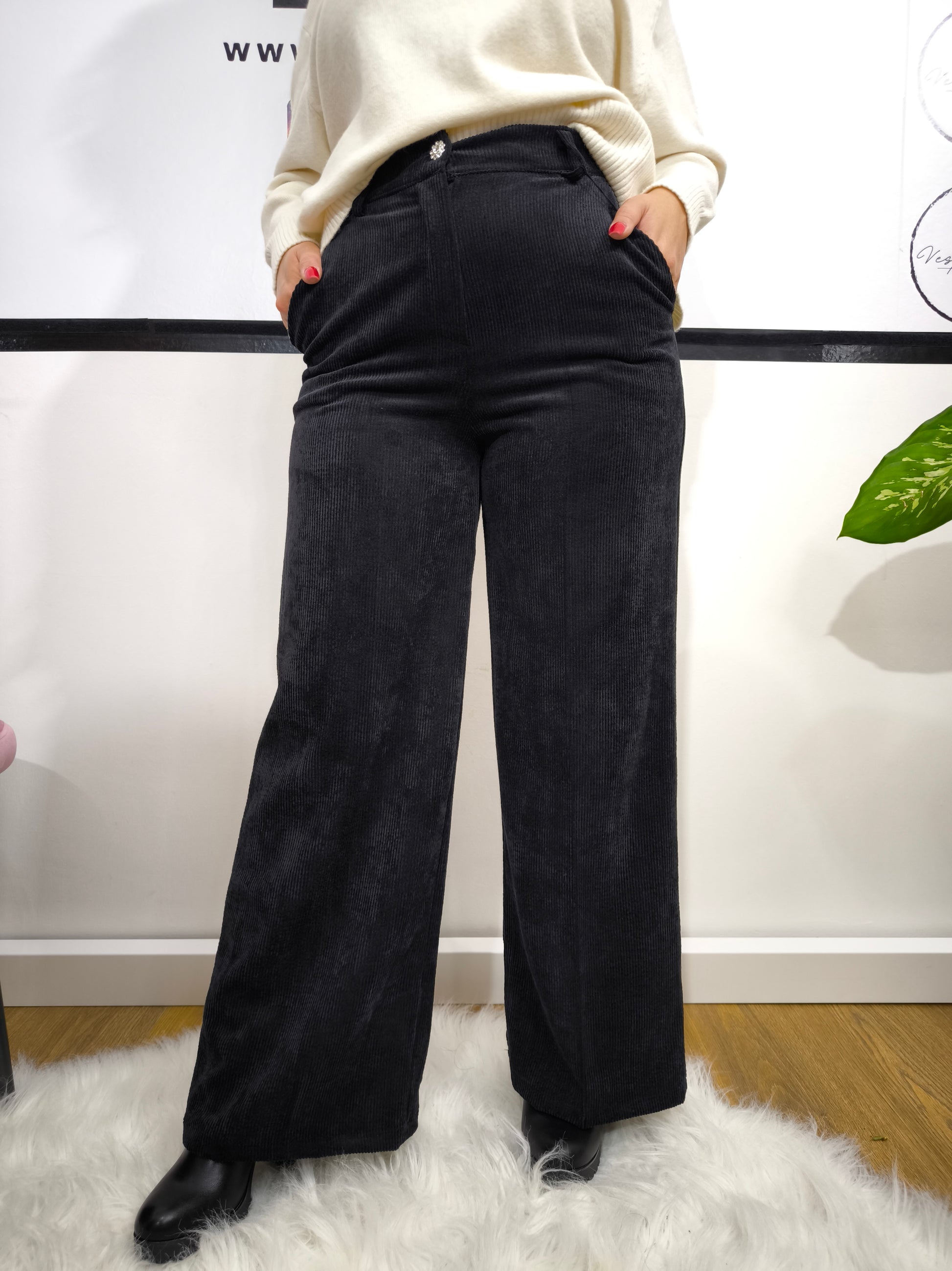 Pantalone in velluto a costine nero con taglio a palazzo indossato da donna con maglione bianco.