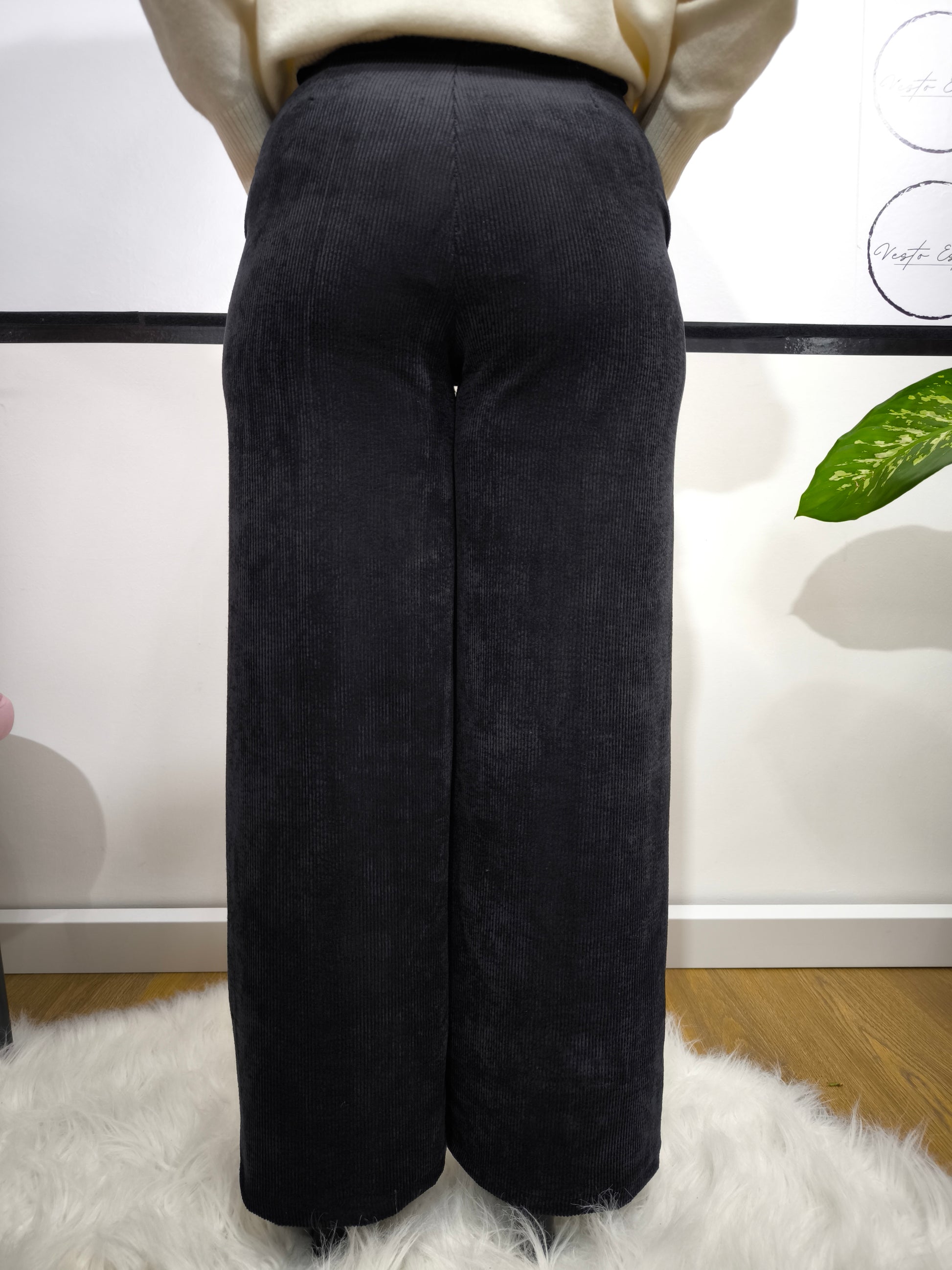 Pantalone in velluto a costine nero con taglio a palazzo indossato da donna con maglione bianco.