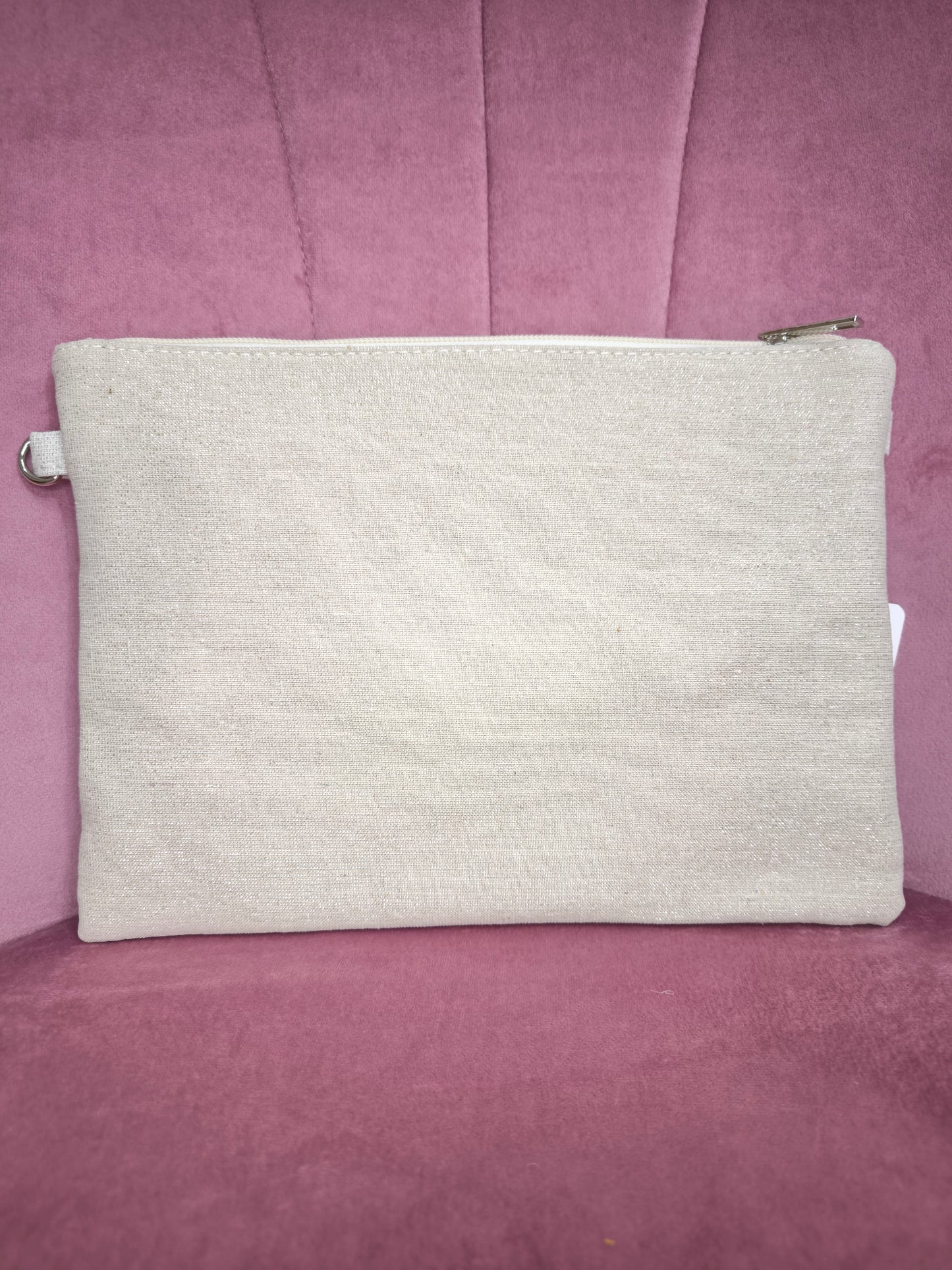 Pochette boho chic con occhio greco portafortuna, decorata con pizzo, conchiglie, piume dorate e dettagli turchesi, appoggiata su una sedia rosa.