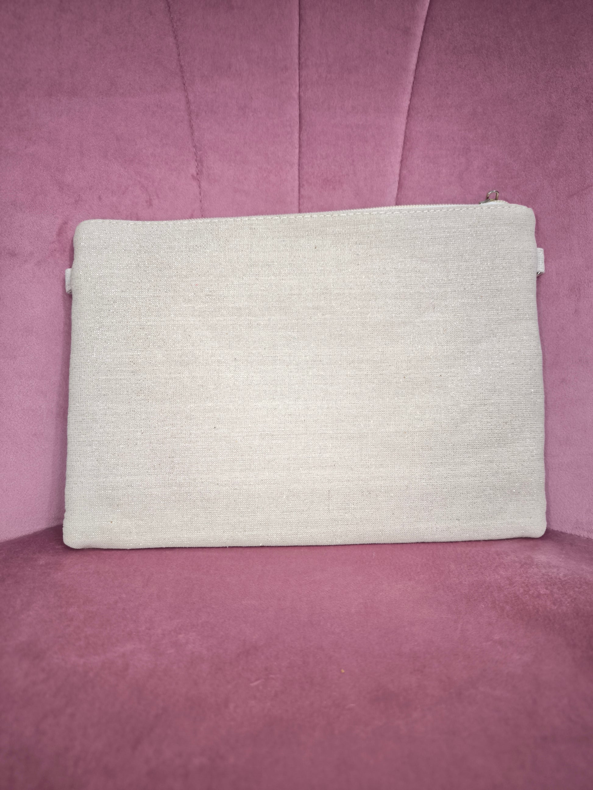 Pochette boho chic con tracolla e polsiera, decorata con pizzo, nappine verde acqua, conchiglie e dettagli dorati, appoggiata su una sedia rosa.