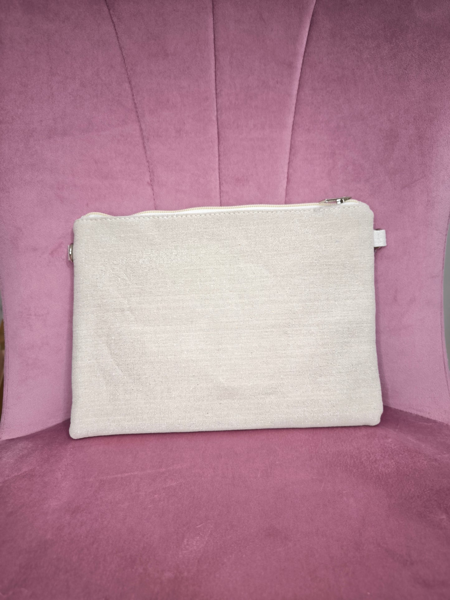 Pochette boho chic con tracolla e polsiera, decorata con pizzo, perline, conchiglie e pietre colorate, appoggiata su una sedia rosa.