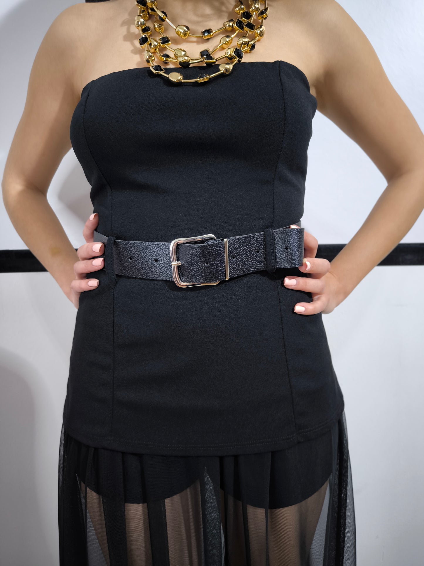 Donna indossa una tutina nera senza spalline con gonnellone in tulle cucito in vita e cintura nera inclusa – look elegante.