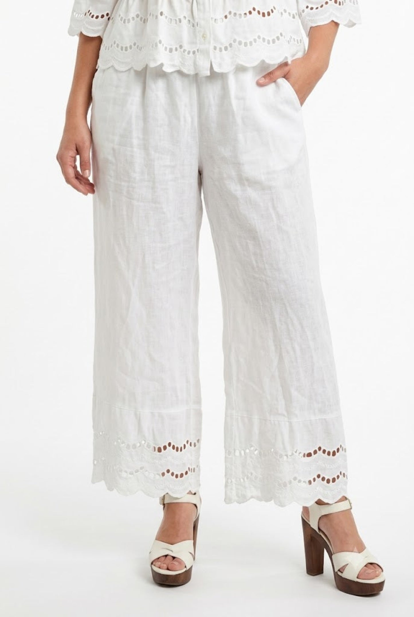 Modella con pantaloni palazzo in puro lino bianco, vita comoda, tasche laterali e fondo ricamato.