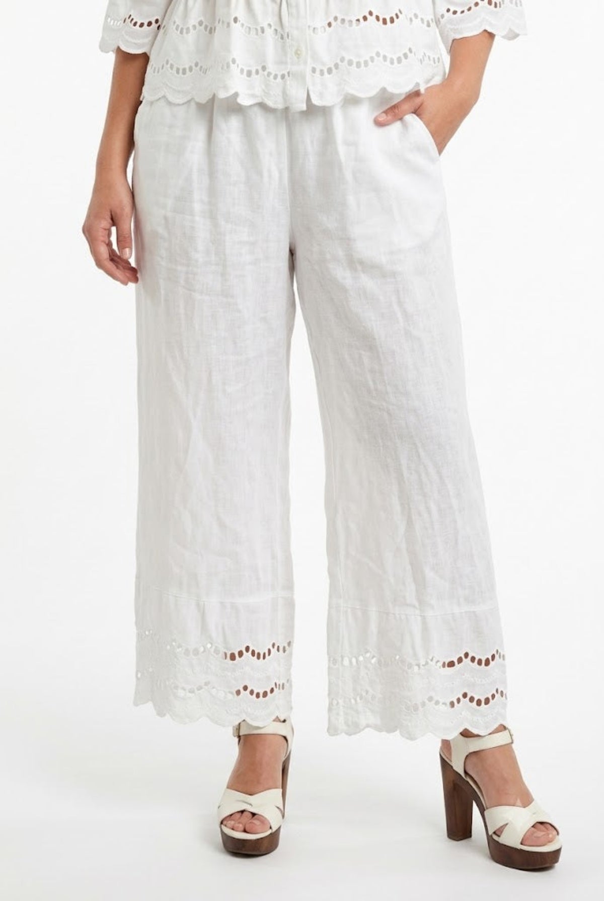 Modella con pantaloni palazzo in puro lino bianco, vita comoda, tasche laterali e fondo ricamato.